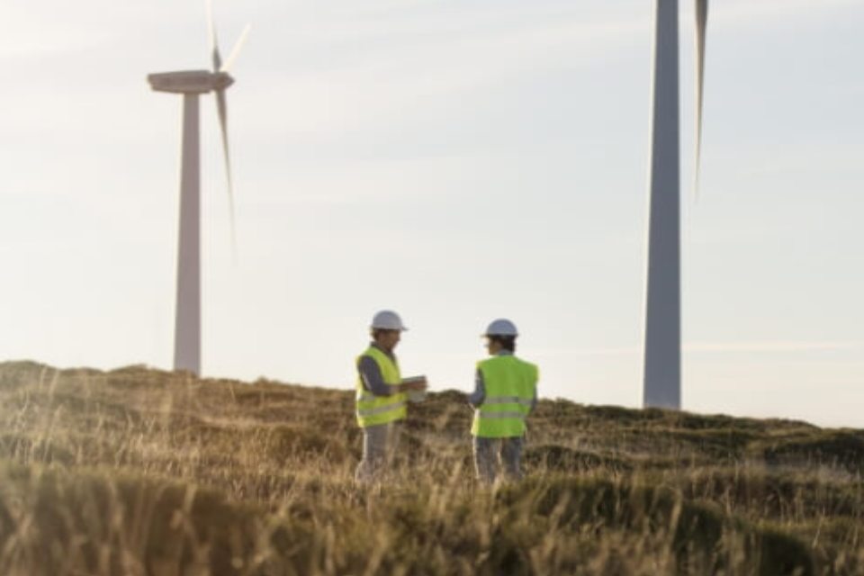 EVIG - Zwei Techniker mit Warnwesten und Bauhelmen stehen in einem Feld, umgeben von Windkraftanlagen